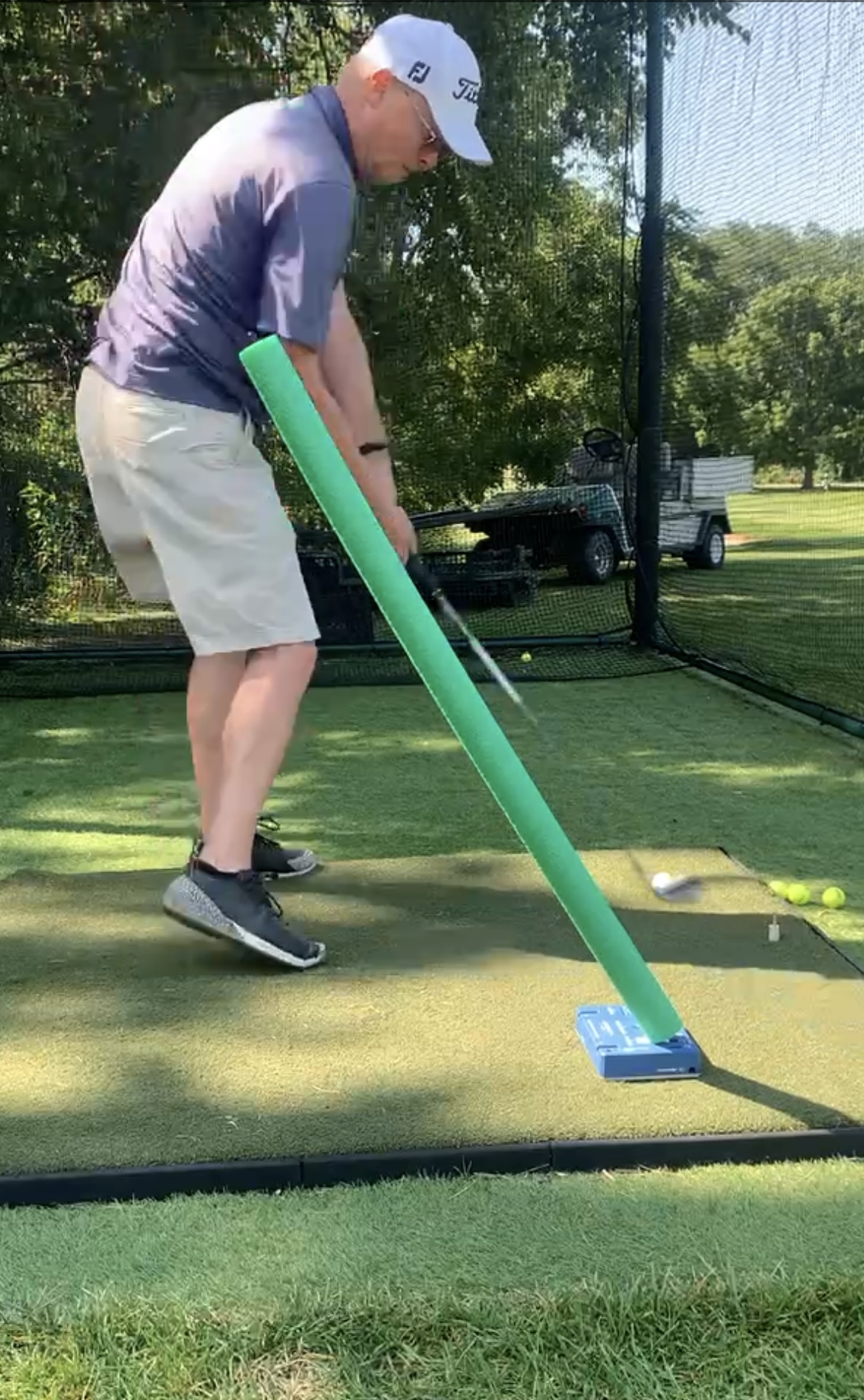 Golfer swinging under an angled foam noodle that constrains the downswing plane